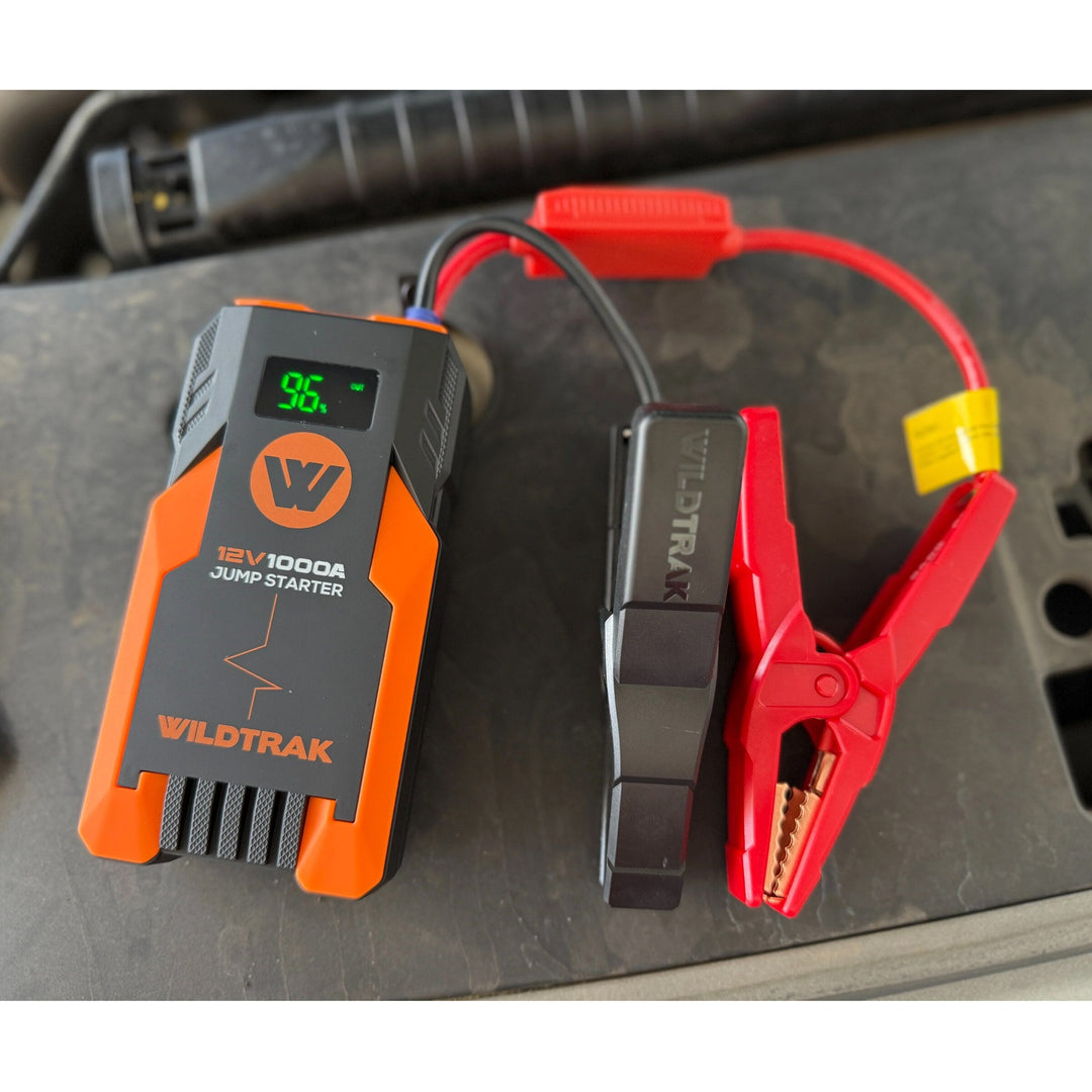 Wildtrak S1000A jump starter and clamps beside a vehicle battery